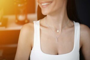 Woman wearing layered silver necklaces, including a vertical bar and a circular pendant.
