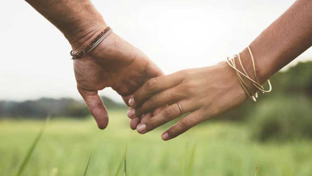 Two people gently holding hands in a field, symbolizing emotional connection and trust.