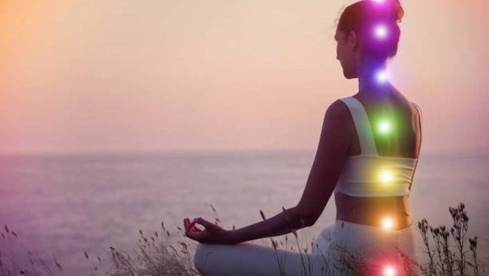 Woman meditating at sunset with glowing chakra points aligned along her spine