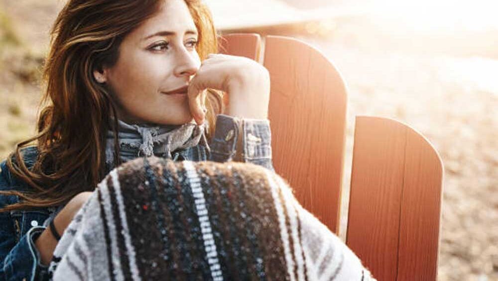 Woman in quiet reflection wrapped in a blanket, gazing softly toward the light