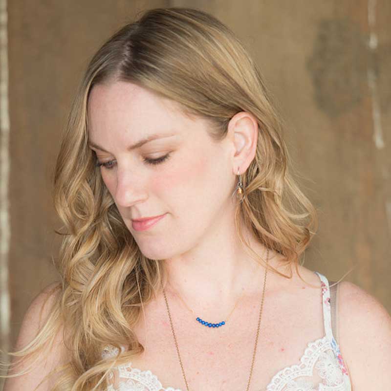 Woman wearing the Circlet Lapis Lazuli Bar Necklace by Saressa Designs layered with a long gold chain.