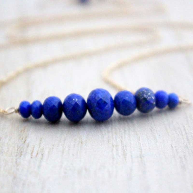 Close-up of a Lapis Lazuli bar necklace featuring faceted rondelle gemstones arranged in a gradient on a gold filled chain by Saressa Designs.