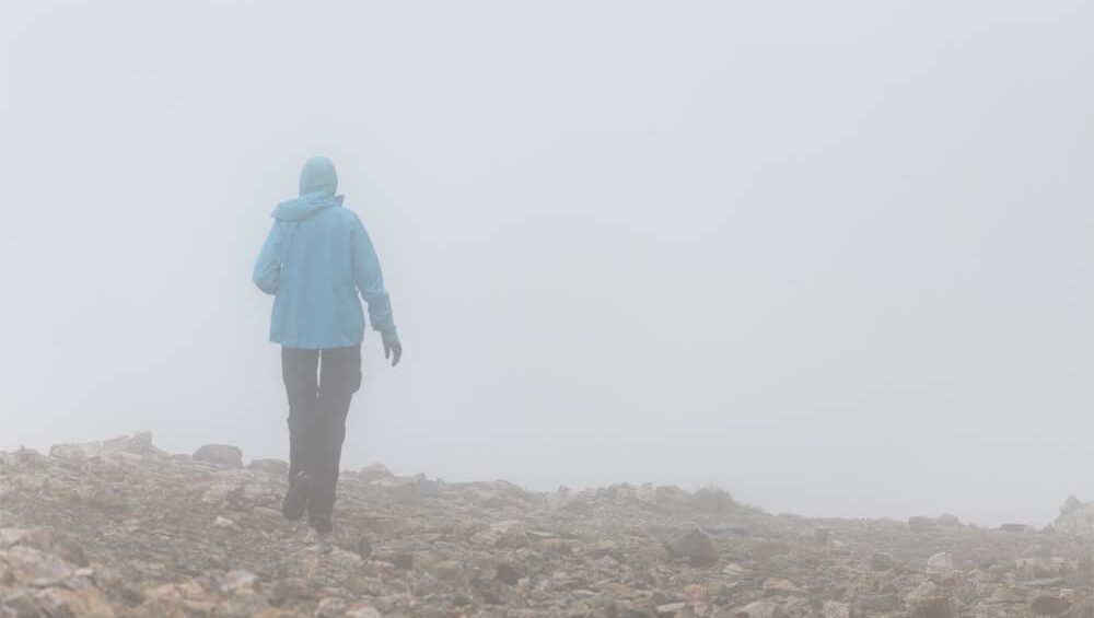 Woman in a blue jacket walking alone through a rocky, fog-covered path—symbolizing solitude, emotional healing, and the journey after a dismissive avoidant breakup