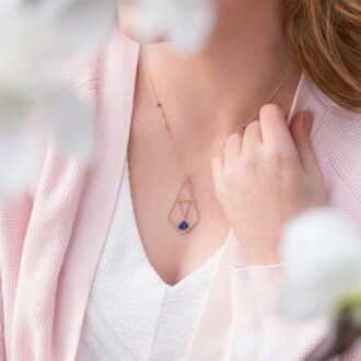 Woman wearing the Peaceful Lapis Symmetry Necklace with a geometric gold pendant and lapis accent