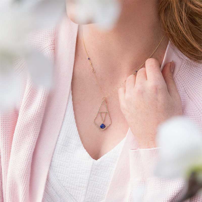 Woman wearing the Peaceful Lapis Symmetry Necklace with a geometric gold pendant and lapis accent