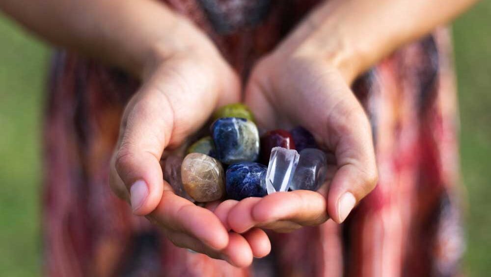 Hands gently holding a variety of colorful raw and polished gemstones in natural light