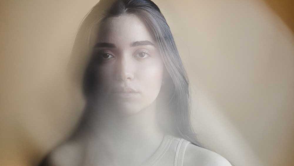 Portrait of a young woman with a distant expression, partially obscured by a soft blur, symbolizing emotional neglect and inner isolation.