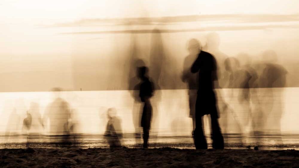 Blurry silhouettes of people on a beach at sunset, symbolizing emotional entanglement and loss of identity in enmeshed relationships.