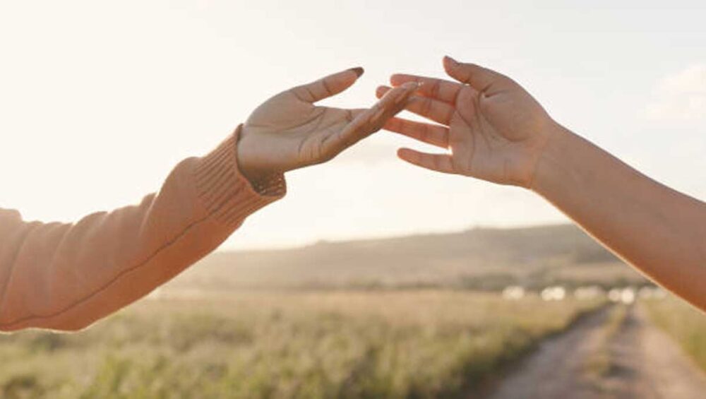 Two hands reaching toward each other in a golden field at sunset, symbolizing emotional connection and empathy