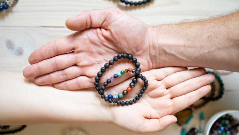 Two hands gently holding chakra bracelets made with healing gemstones, symbolizing energy balance and connection.