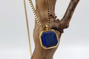 Gold necklace with lapis lazuli gemstone pendant hanging from natural wood – Middle Eastern jewelry style