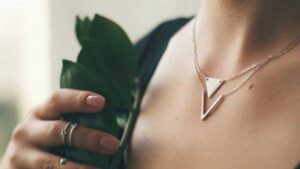 Close-up of woman wearing minimalist geometric triangle necklace and rings, holding a green leaf