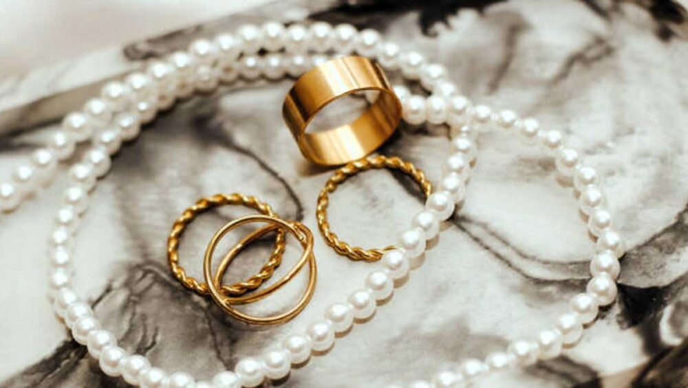 Flat lay of gold rings and pearl necklace on marble background symbolizing jewelry as self-expression.