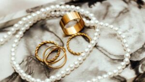Flat lay of gold rings and pearl necklace on marble background symbolizing jewelry as self-expression.