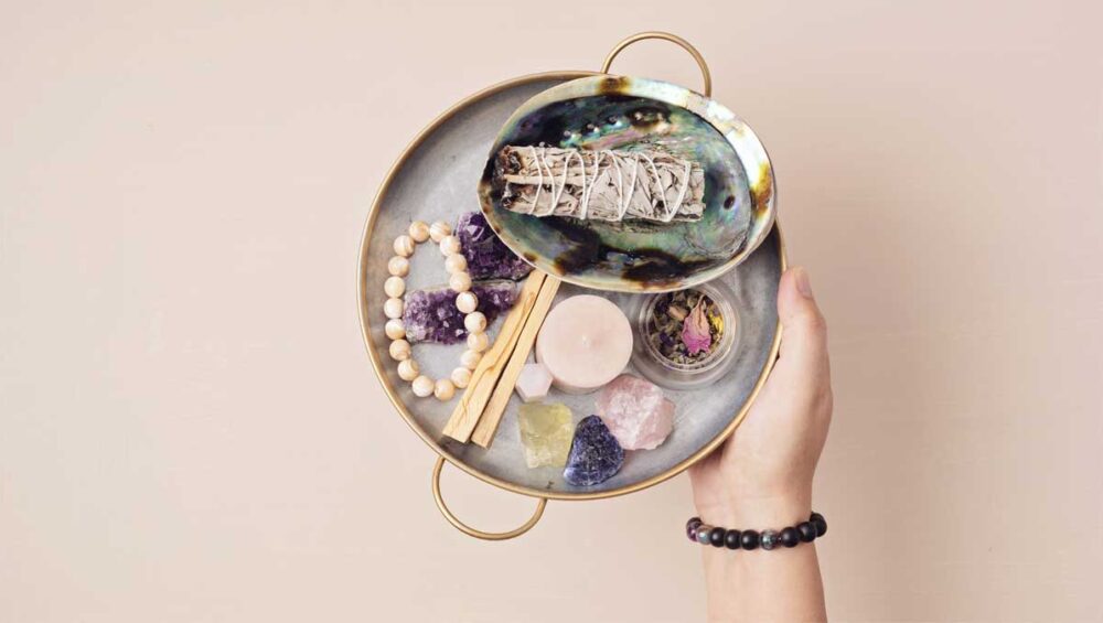 Jewelry and mindfulness tools with crystals, bracelet, sage, and candle on a neutral background.