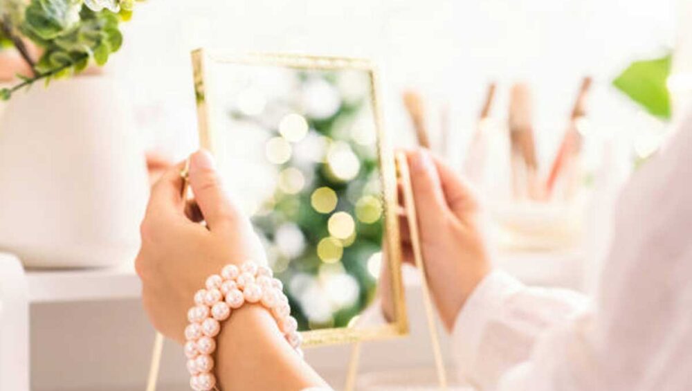 Woman holding a mirror with pearl bracelets on her wrist, symbolizing self-reflection and personal expression through jewelry.