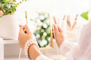 Woman holding a mirror with pearl bracelets on her wrist, symbolizing self-reflection and personal expression through jewelry.