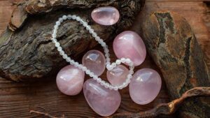 Rose quartz stones and beaded necklace resting on rustic wood and bark, symbolizing jewelry as emotional expression