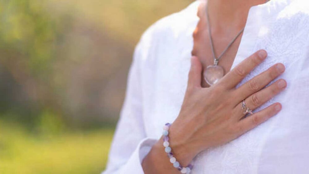 Close-up of a hand over heart wearing a beaded bracelet and crystal necklace, symbolizing grounding and calm through meaningful jewelry.