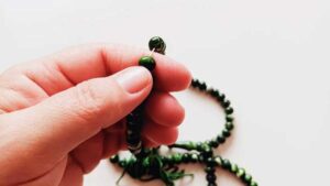 Close-up of a hand gently holding a green beaded necklace, capturing the tactile connection to jewelry.