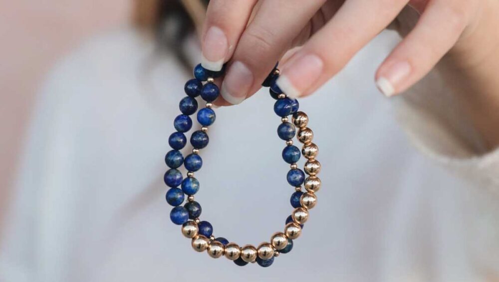 Hand holding a lapis lazuli bracelet with deep blue and gold beads, symbolizing truth and protection