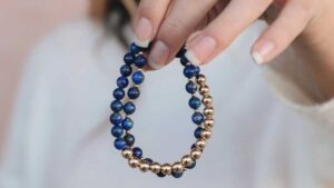 Hand holding a lapis lazuli bracelet with deep blue and gold beads, symbolizing truth and protection
