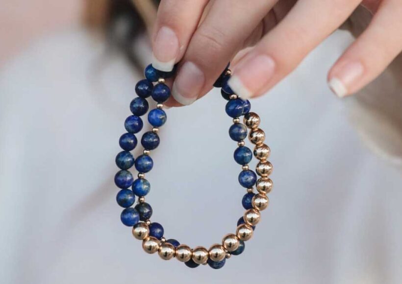 Hand holding a lapis lazuli bracelet with deep blue and gold beads, symbolizing truth and protection