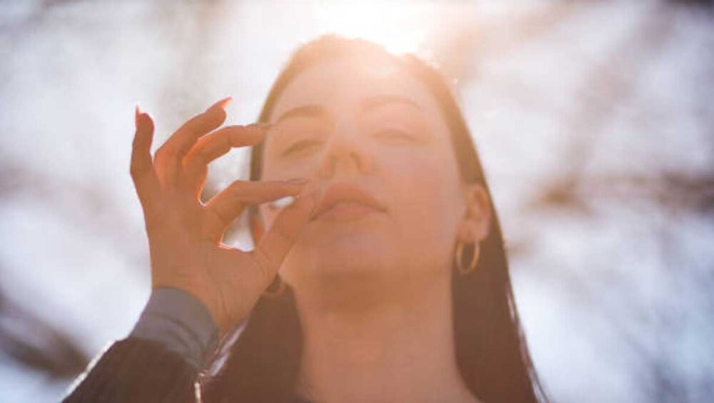 Woman with hand at lips and sunlight behind her, symbolizing inner voice, healing, and intuitive empowerment.