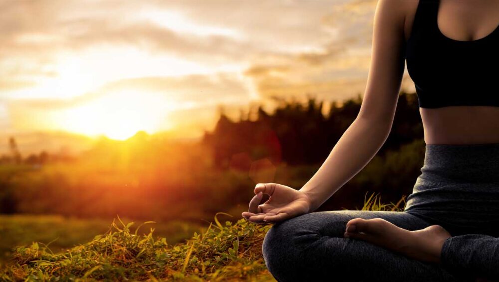 Woman meditating outdoors at sunrise, practicing mindfulness for stress relief