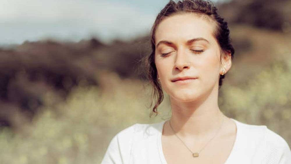 Woman peacefully meditating outdoors with eyes closed, practicing mindfulness in nature.