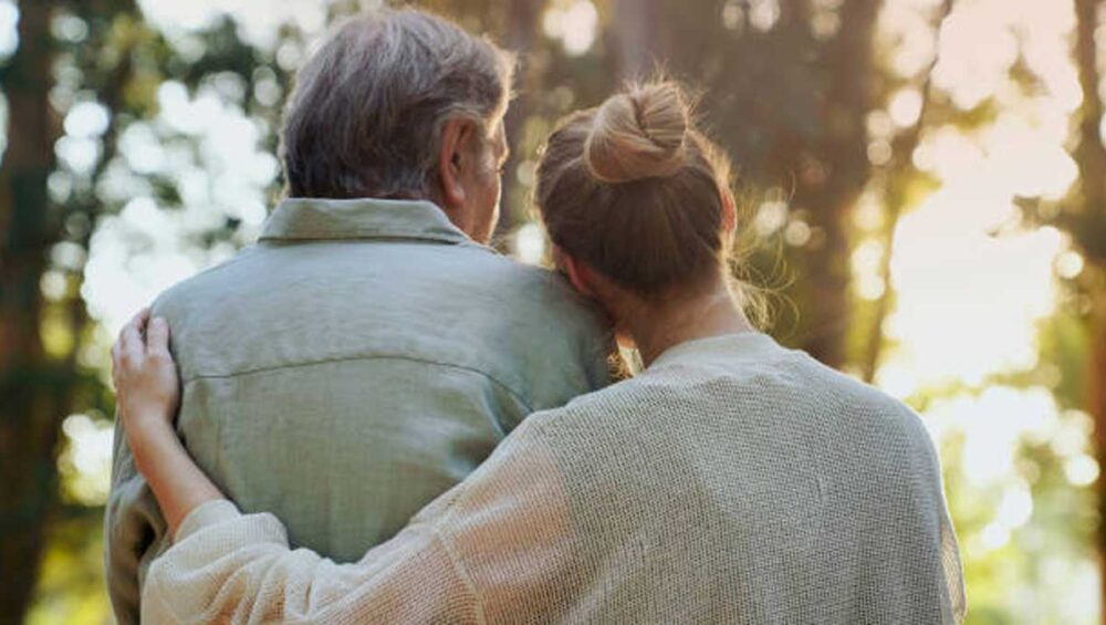 Woman embracing older man in a forest, showing compassion and support