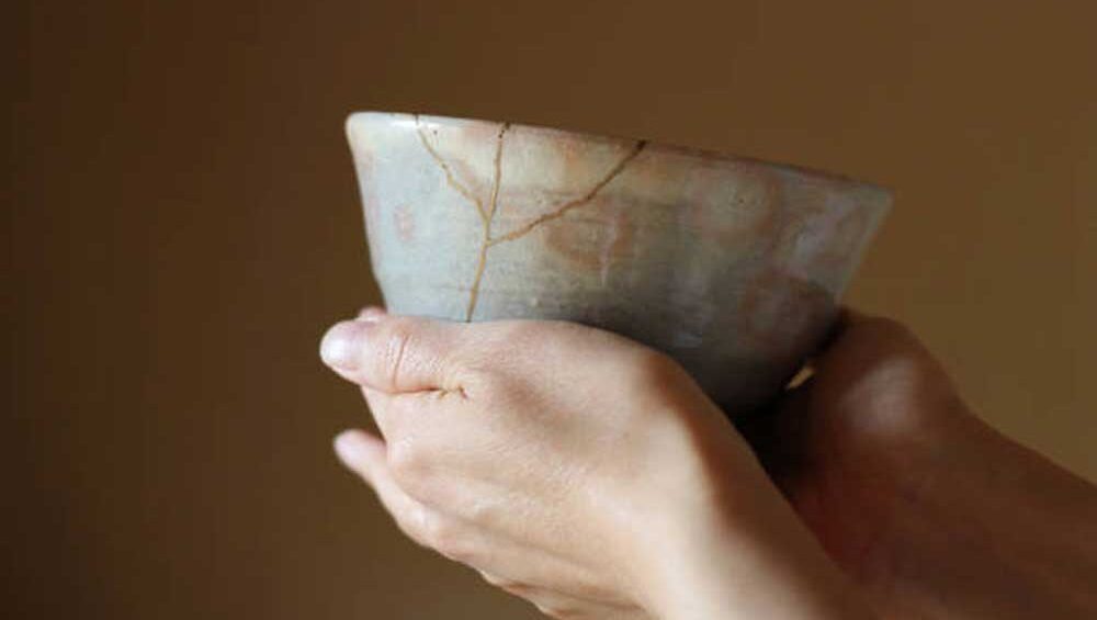 Hands holding a cracked ceramic bowl repaired with golden joinery, symbolizing wabi-sabi