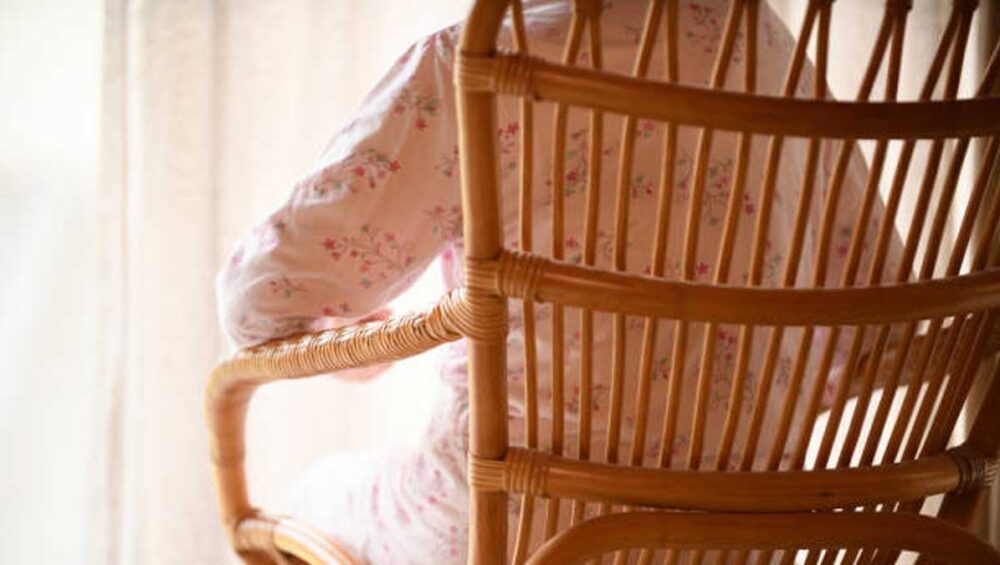 Woman sitting in a wooden rocking chair facing away, symbolizing emotional distance and silence in a mother-daughter relationship