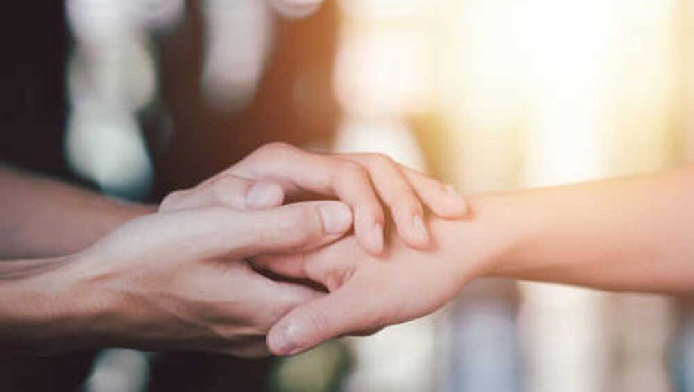 Two hands gently holding an arm, symbolizing emotional support and empathy in a soft, warm light.