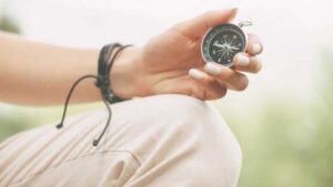 Woman holding a compass in her hand, wearing a black leather wrap bracelet, symbolizing inner direction and self-discovery through jewelry.