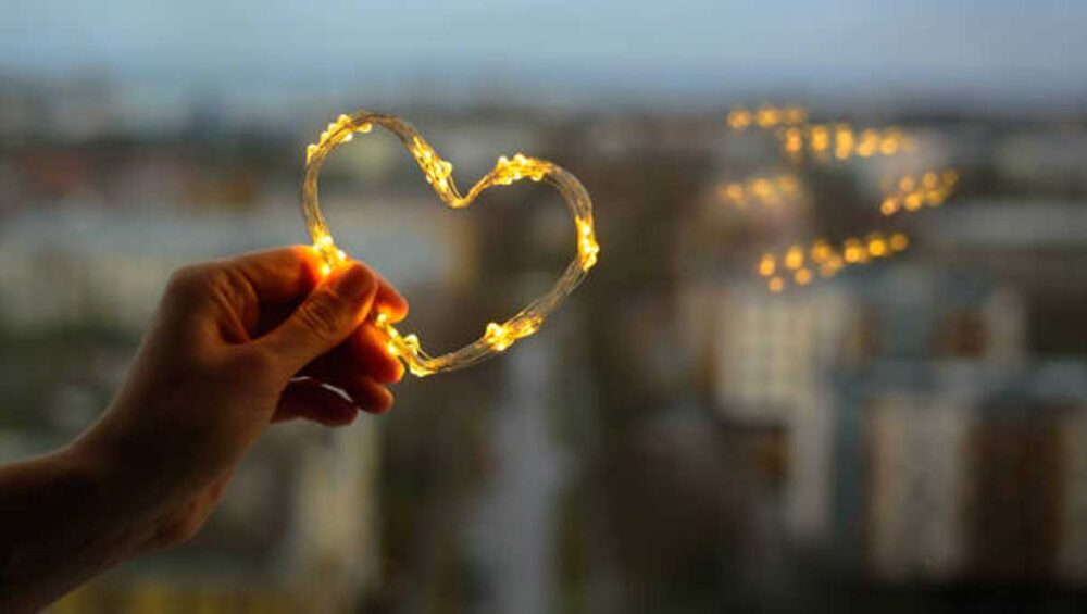 Hand holding glowing heart-shaped lights against blurred cityscape, symbolizing emotional healing and connection