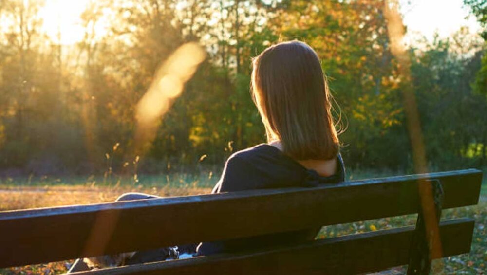Woman sitting on a bench at sunset, reflecting in solitude, symbolizing healing from emotional neglect and erasure