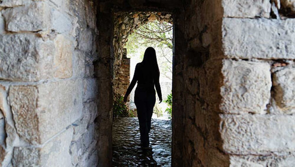 Woman walking out of a dark stone passage into light, symbolizing breaking free from gaslighting in narcissistic families