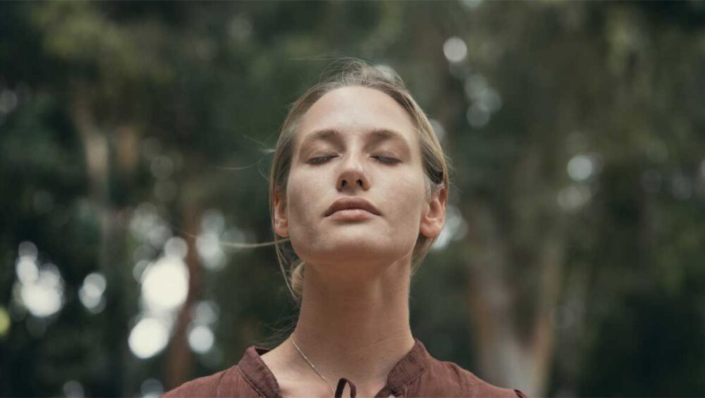 Woman with eyes closed practicing emotional self-awareness outdoors, symbolizing introspection and personal growth for avoidants.