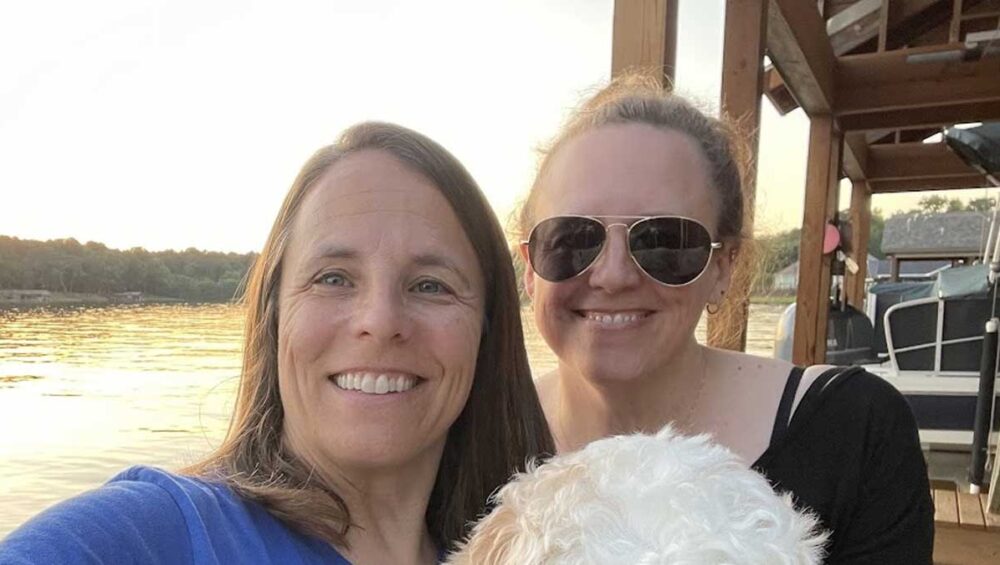 Two sisters smiling together outdoors near the water at sunset