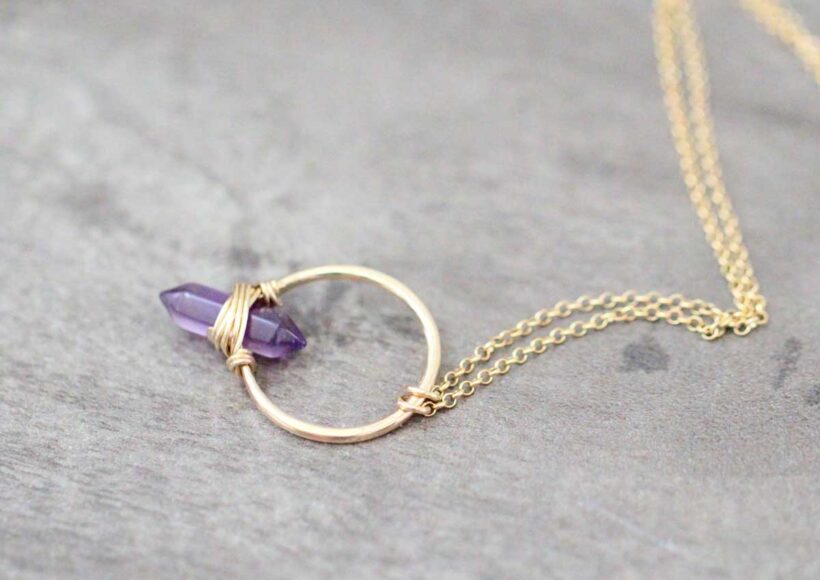 Gold-filled hoop necklace with a wire-wrapped amethyst point, flat lay on gray background