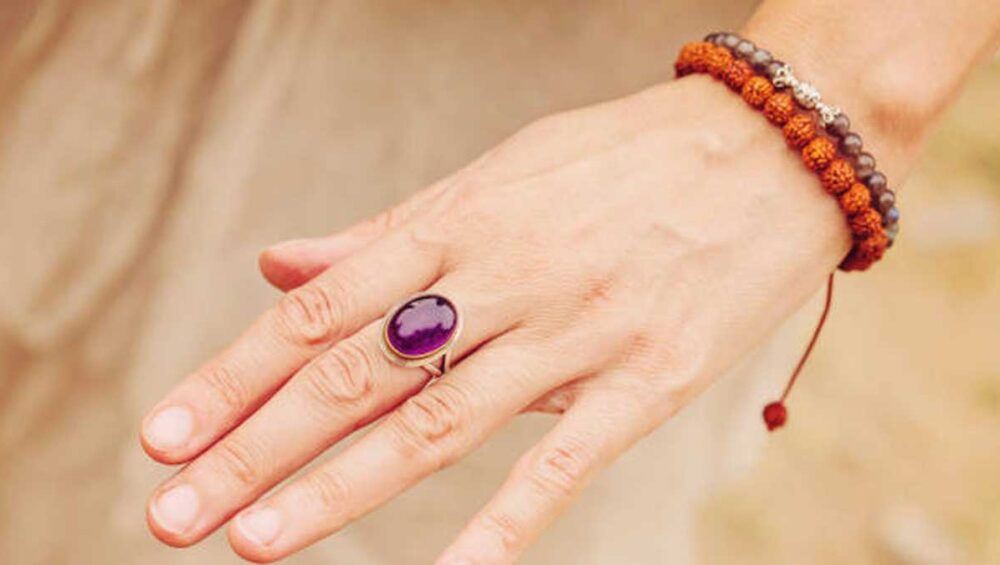 Hand wearing an amethyst ring and beaded bracelet, symbolizing intention-driven jewelry and mindful energy.