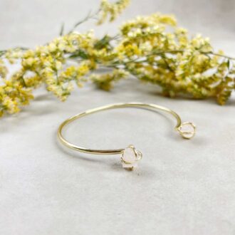 Gold cuff bracelet with two raw rose quartz nuggets on each end, displayed with yellow flowers.