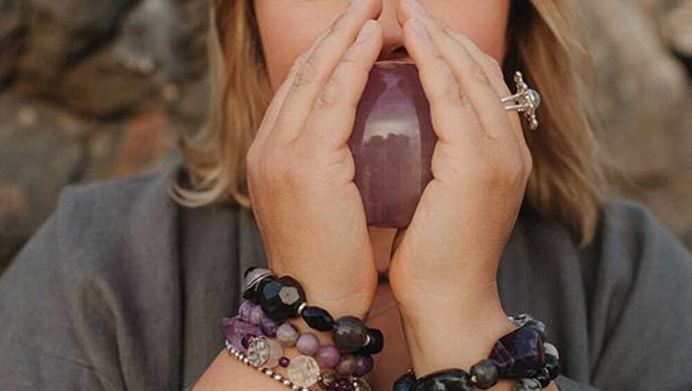 Woman wearing gemstone healing bracelets while holding an amethyst crystal for energy and balance