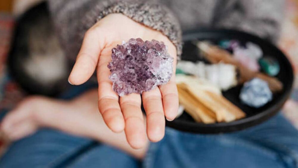 hand holding amethyst crystal cluster for healing with gems