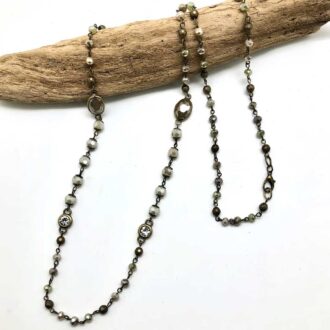 Antique hematite and glass bead chain necklace with oval glass accents and faceted beads displayed on driftwood.
