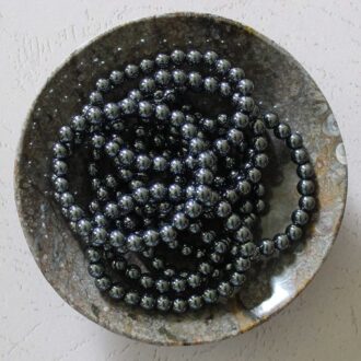 Hematite beaded bracelet displayed in a stone dish, polished for a sleek metallic finish.