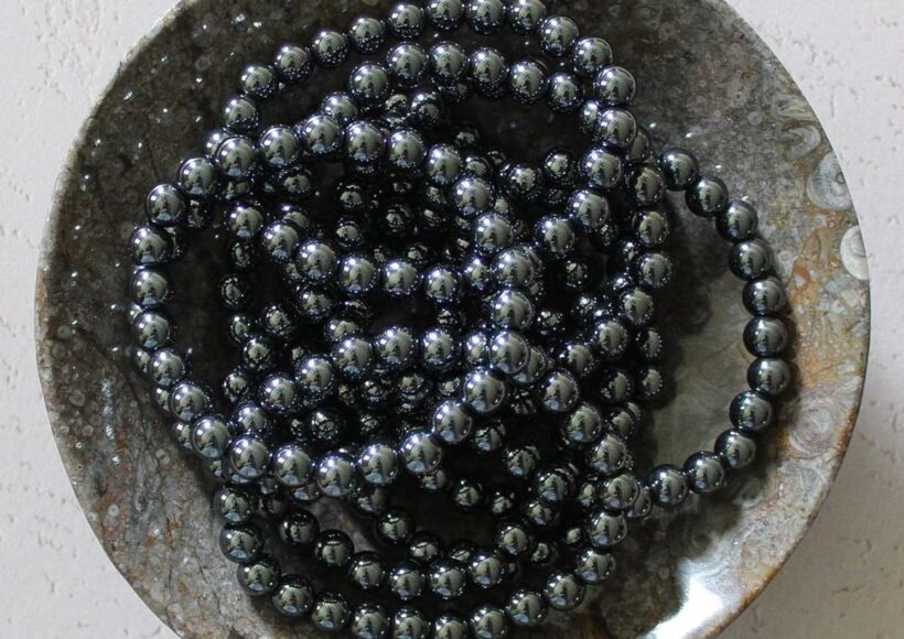 Hematite beaded bracelet displayed in a stone dish, polished for a sleek metallic finish.