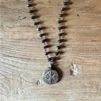 Old world hematite necklace with faceted bead chain and antique-style two-sided pendant on wood background.