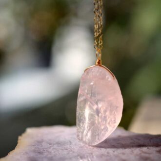 Raw rose quartz crystal pendant necklace on a gold chain.